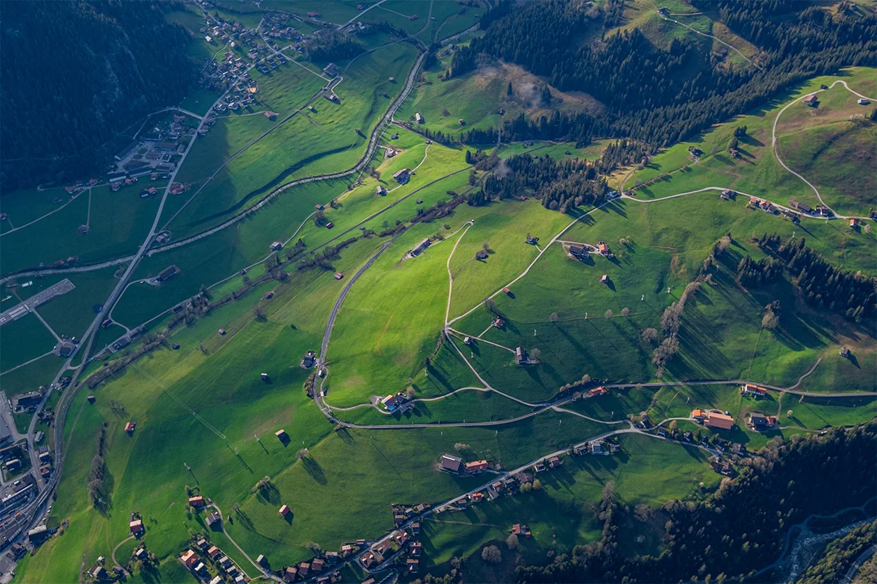 Vue aérienne d'une vallée alpine verdoyante parsemée de hameaux