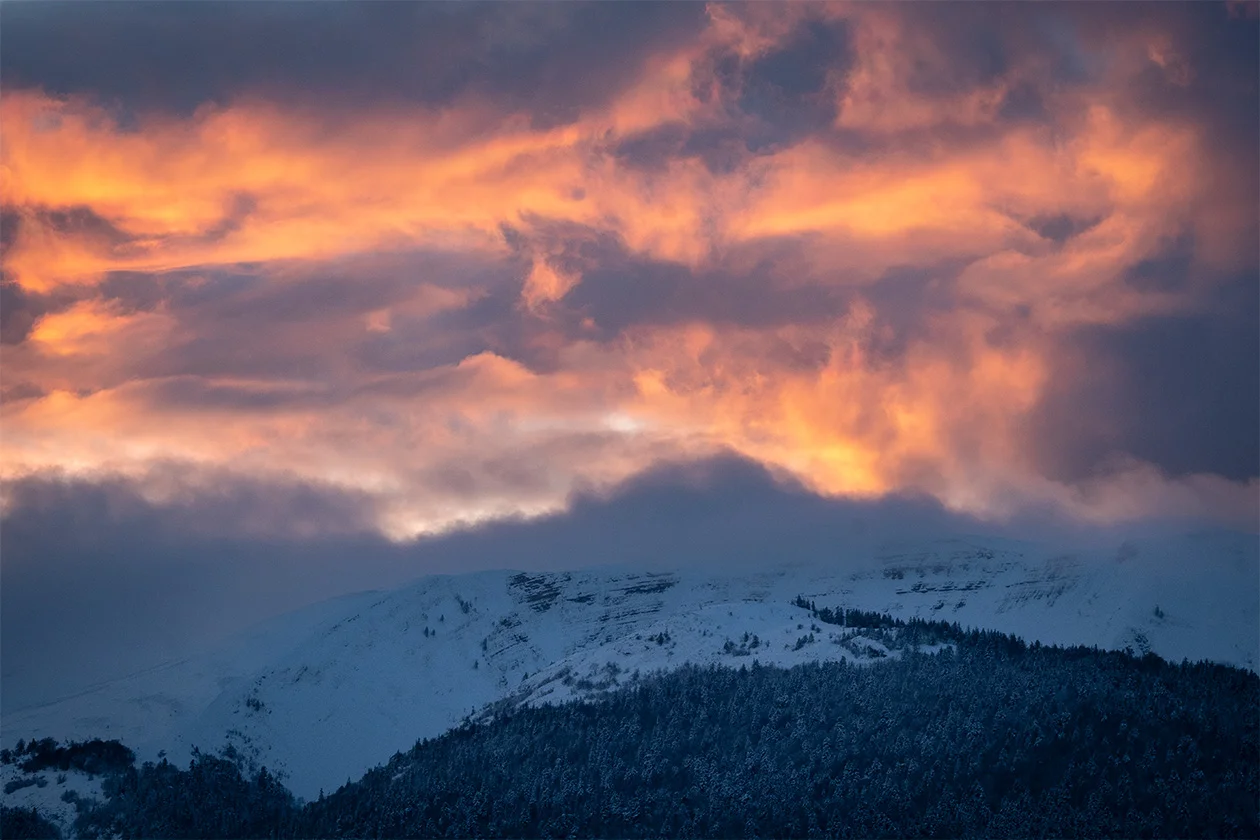 Coucher de soleil enflammé sur les sommets enneigés, nuages oranges au-dessus de la vallée