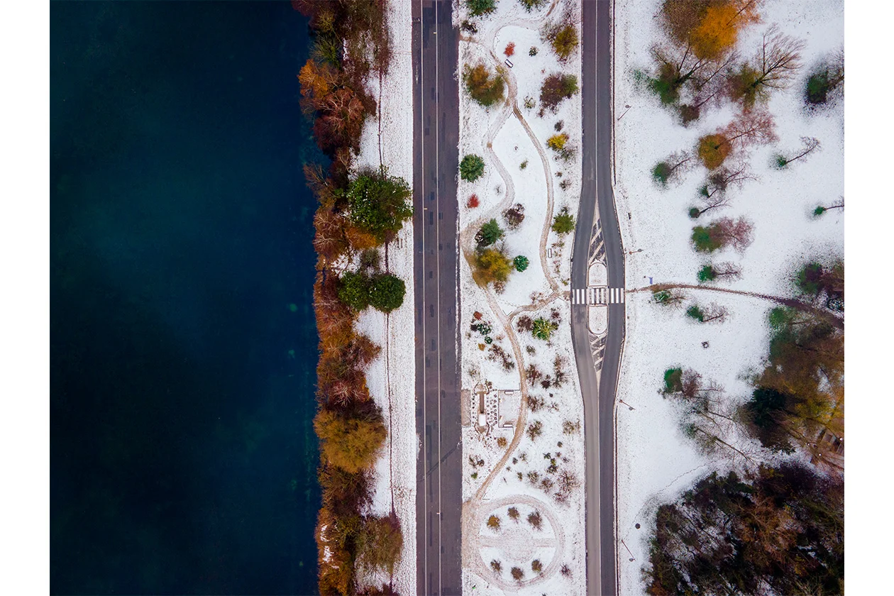Vue aérienne d'un parc enneigé entre une rivière sombre et des chemins en hiver