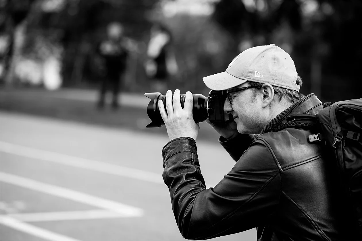 Photographe en action en noir et blanc visant son sujet, casquette et veste en cuir