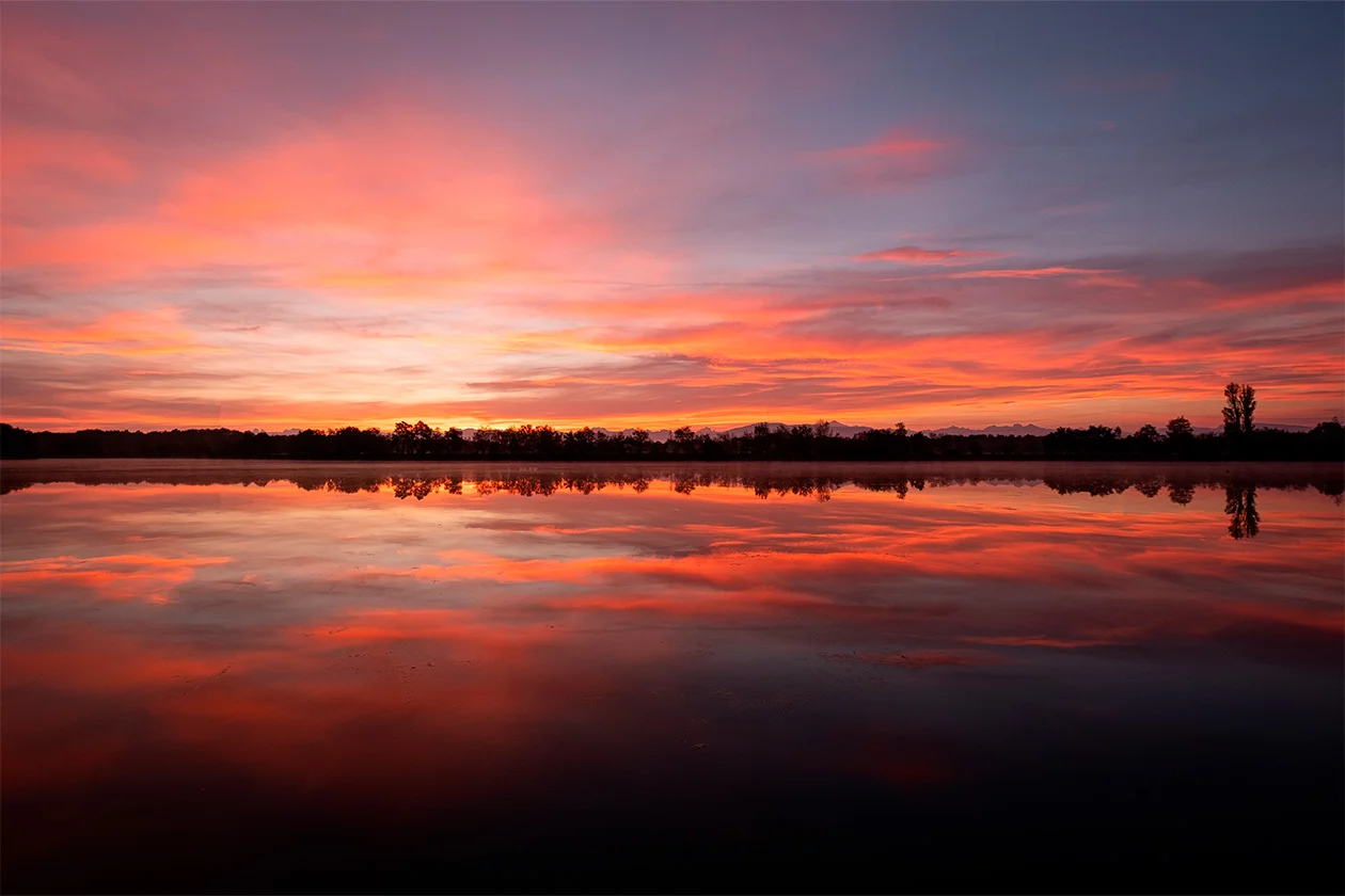 Coucher de soleil rose et orangé reflété sur les eaux calmes d'un lac