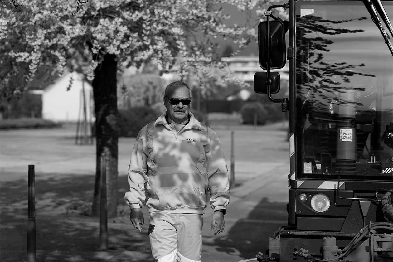 Portrait noir et blanc d'un agent communal en tenue de travail devant un véhicule de chantier