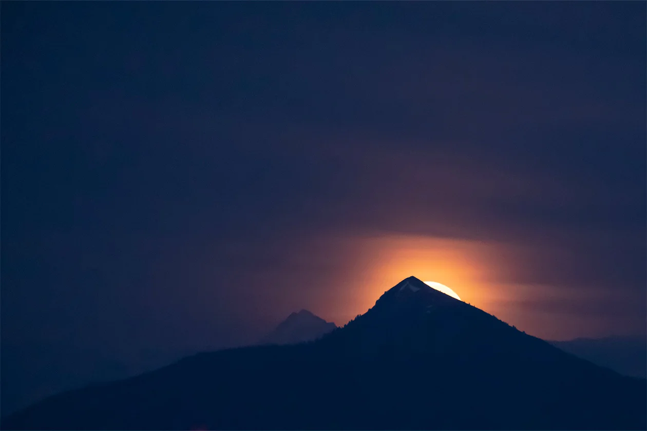 Lever de pleine lune orange derrière une silhouette de montagne sous un ciel violet
