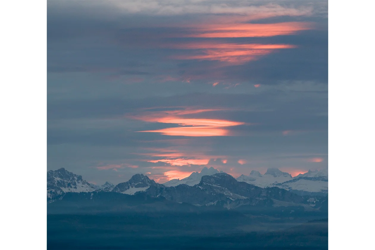 Coucher de soleil sur la chaîne des Alpes vue depuis la vallée, nuages orangés