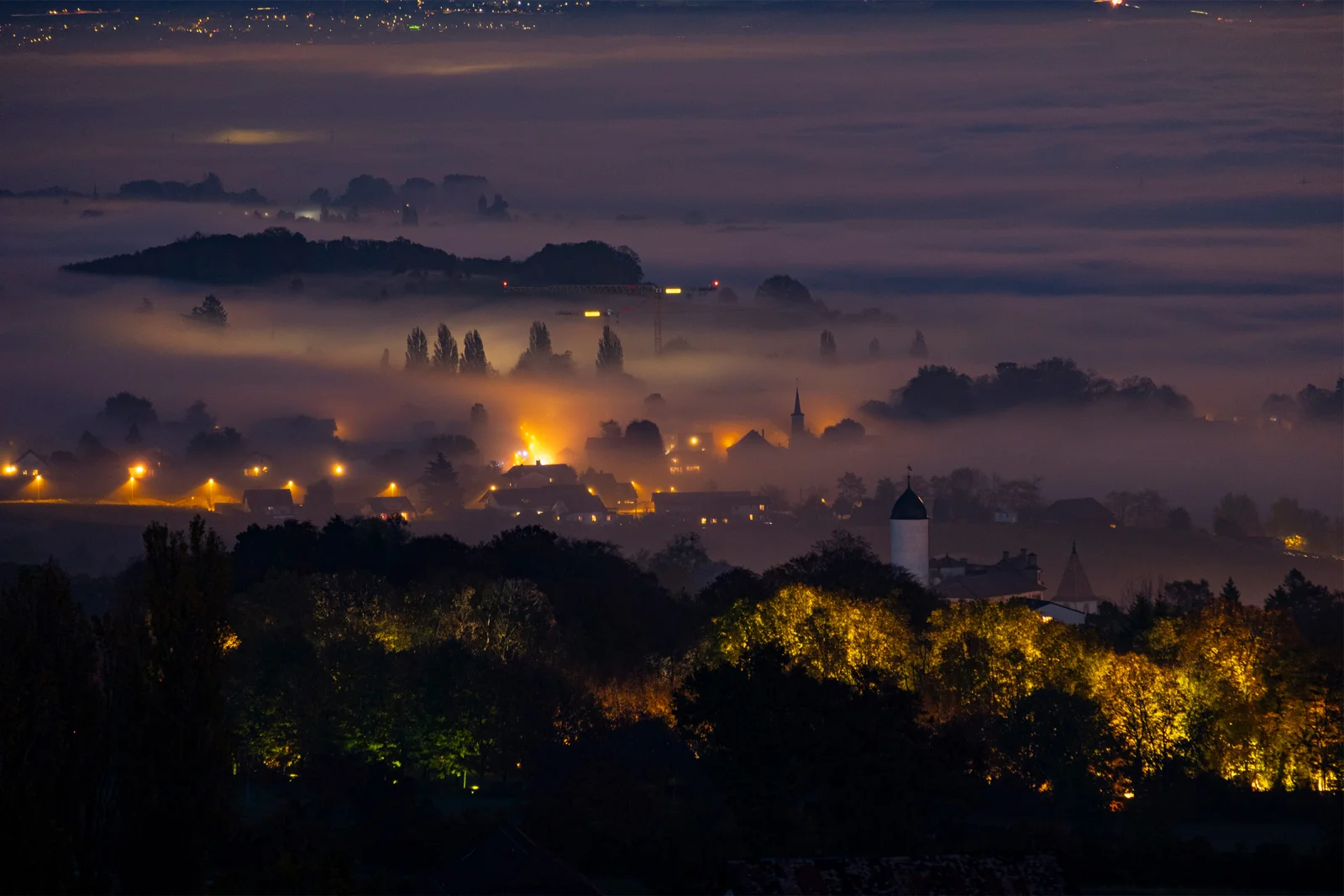 Village suisse plongé dans une brume nocturne dorée, lampadaires illuminant le brouillard