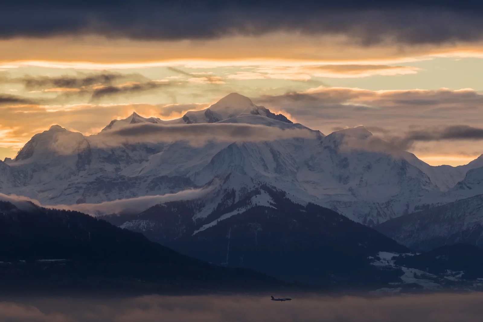 Mont-Blanc dans les nuages dorés au coucher de soleil, avion de ligne survolant la vallée