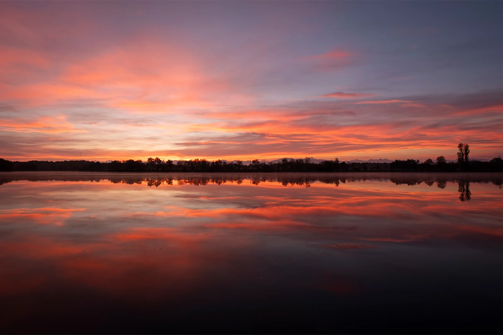 Coucher de soleil rose et orangé reflété sur la surface immobile d'un lac, ciel embrasé