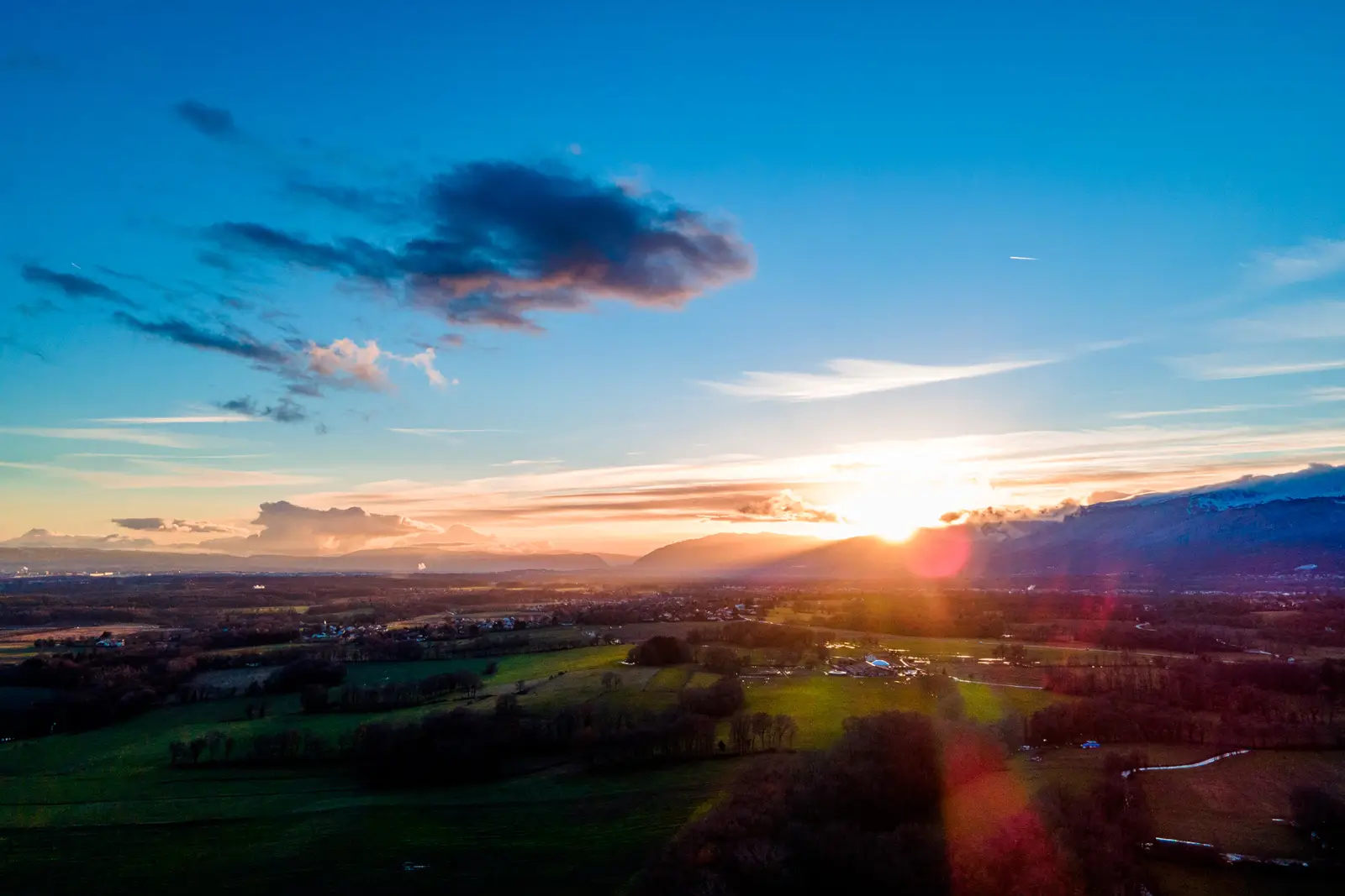 Vue aérienne d'une vallée au coucher du soleil, dernier rayon derrière les montagnes et halo lumineux sur la campagne