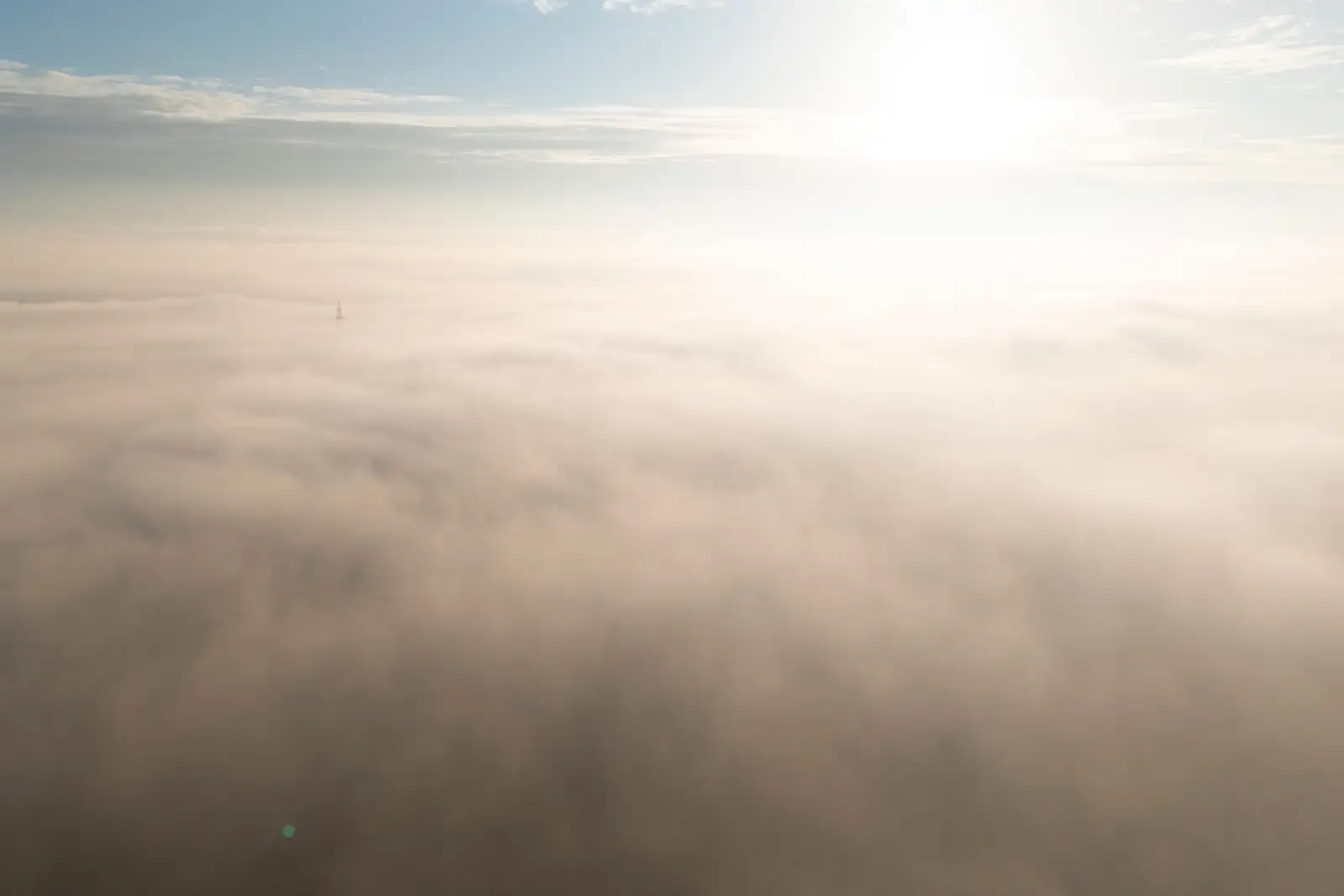 Vue aérienne d'une mer de brouillard au lever du soleil, pylône électrique émergeant à peine de la nappe cotonneuse