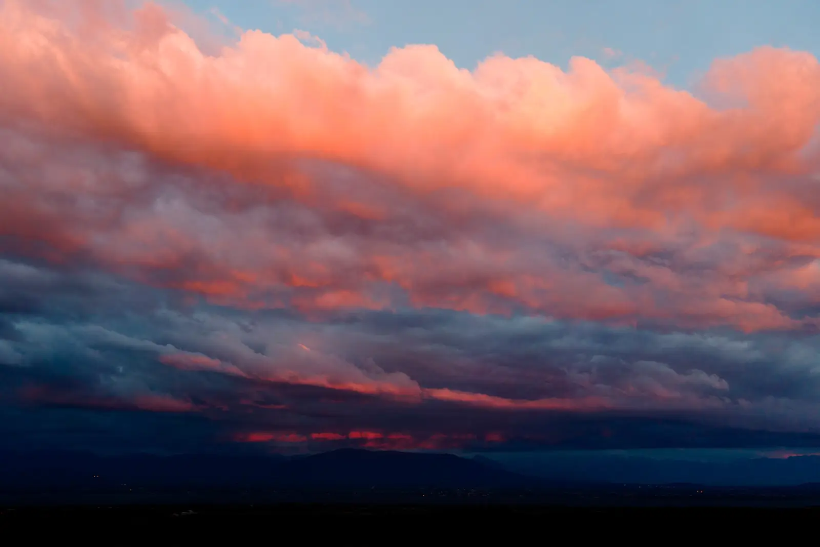 Masse de nuages embrasés de rose et d'orange au crépuscule, au-dessus d'une chaîne de montagnes dans la pénombre