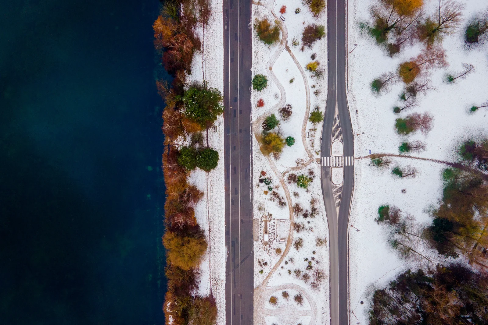 Vue aérienne d'une route enneigée bordée d'une rivière sombre et d'un parc en hiver