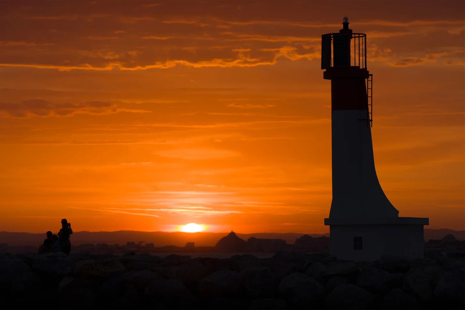 Phare en silhouette devant un coucher de soleil orange flamboyant, observateurs au premier plan